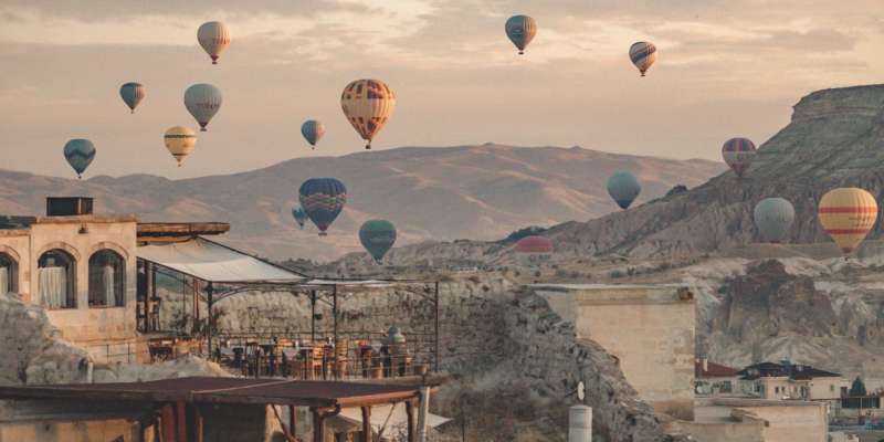 A beautiful view of colorful hot air balloons floating in the sky above the buildings and mountains.